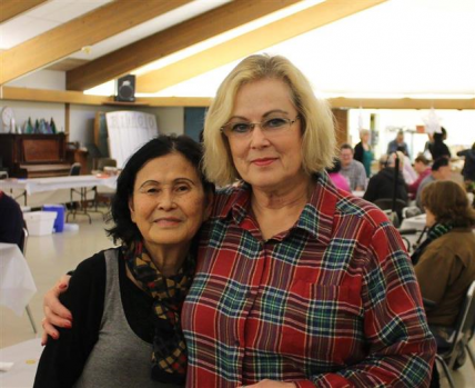 Two female volunteers embrace each other and smile softly for the camera at an event inside the Community room at Center Park. 